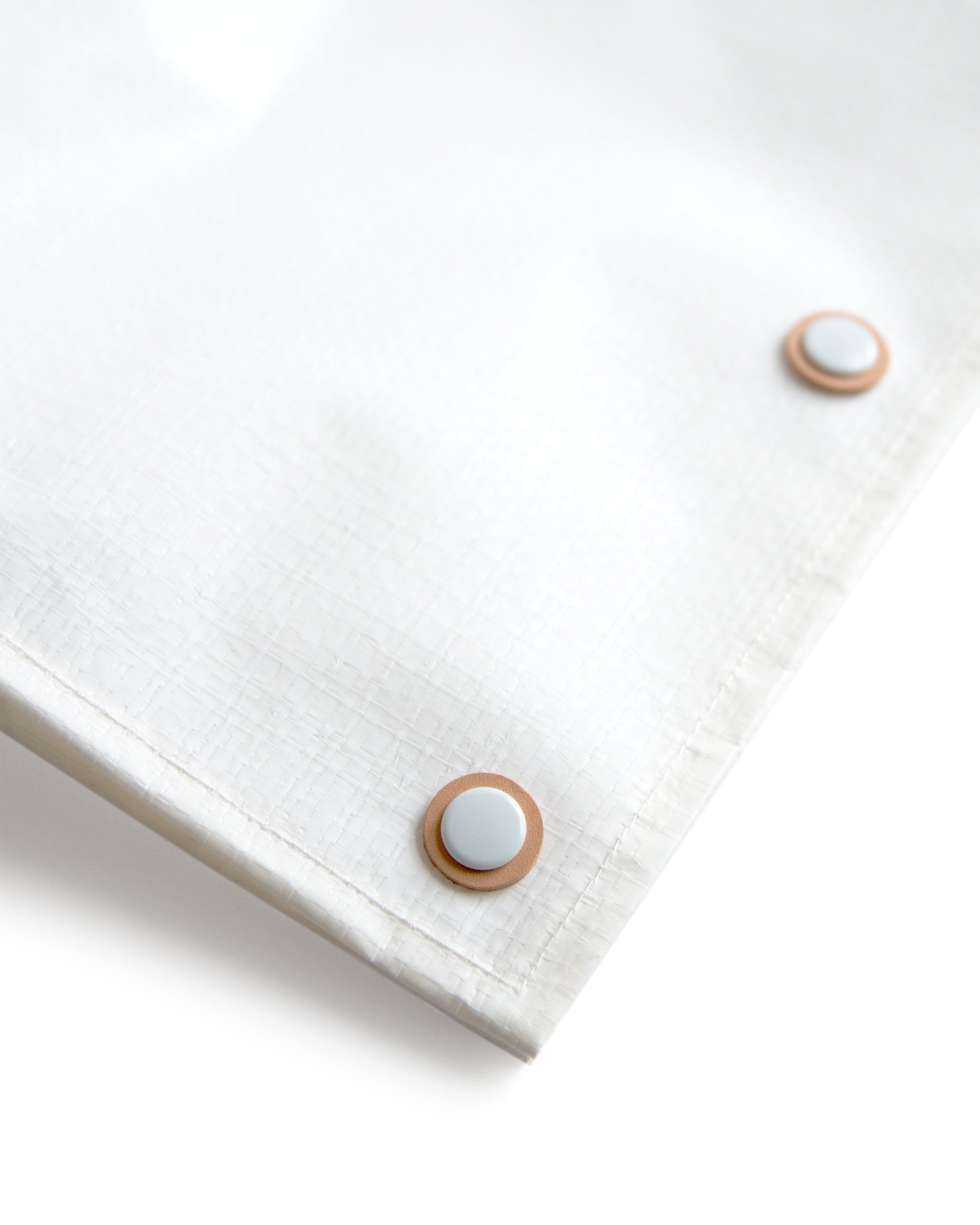 Detail image of the snaps for the hender scheme picnic bag. Each snap is coated in white and is layered on top of a ring of hender scheme signature cow leather.