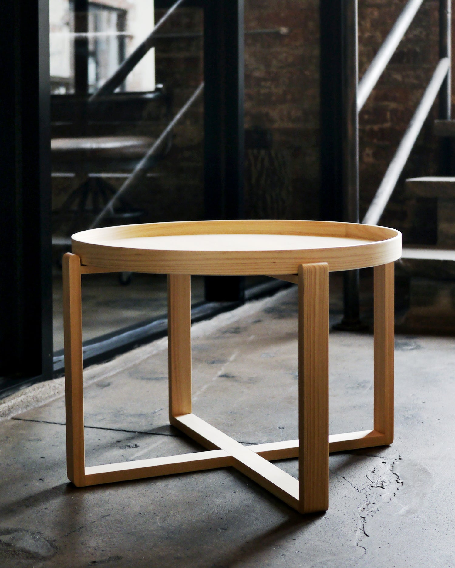 Hinoki magewa tray table placed on a cement floor, with dark brick wall and steel frames and stairs in the background.
