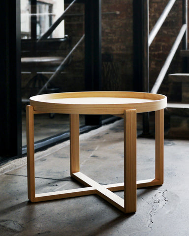 Hinoki magewa tray table placed on a cement floor, with dark brick wall and steel frames and stairs in the background.