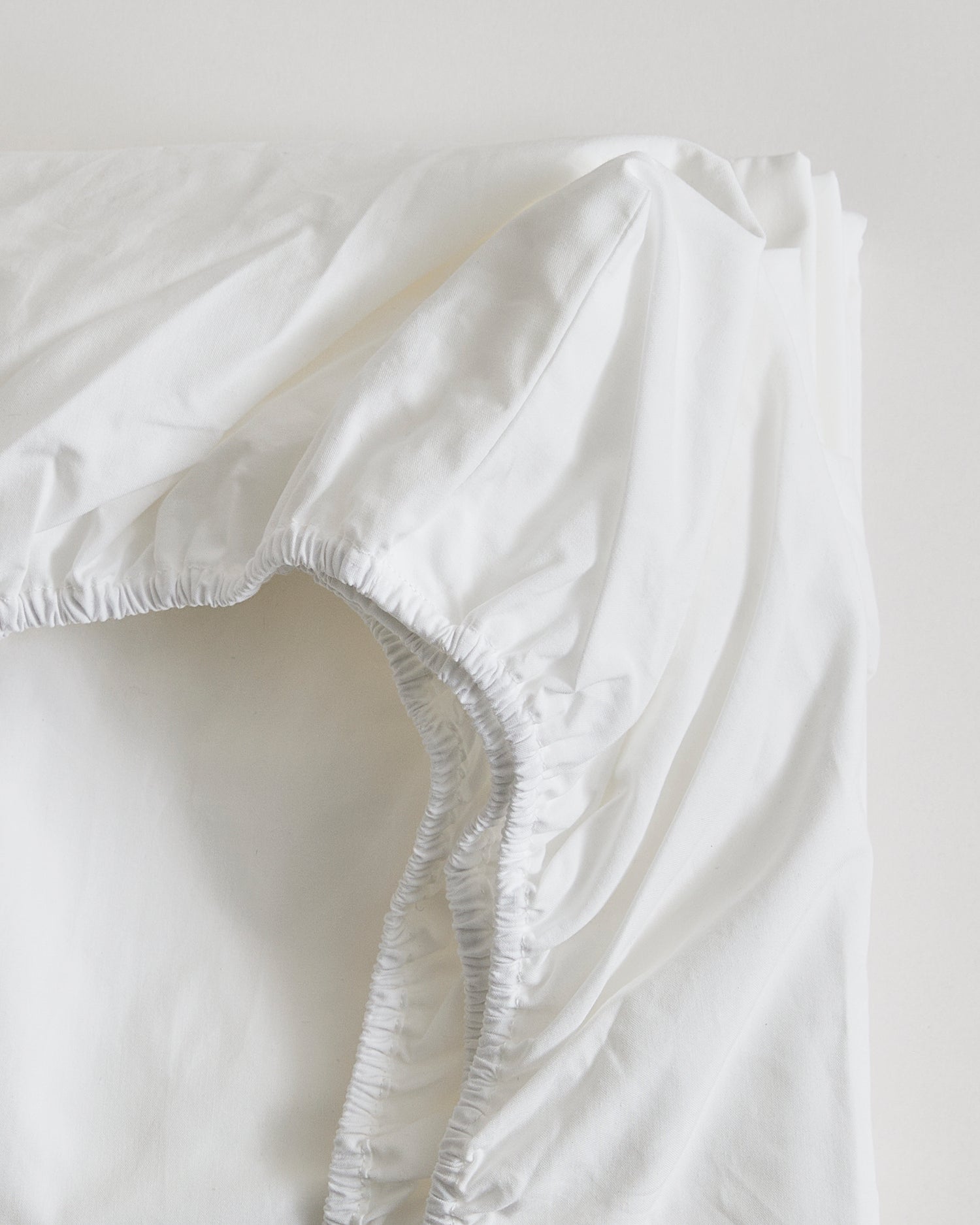 Up-close of white fitted sheet on a gray background