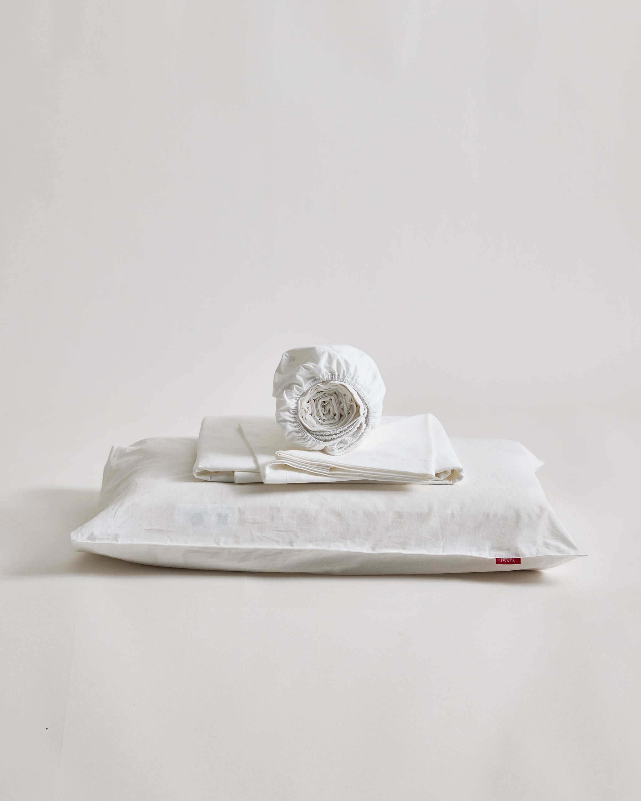 White cotton sheet set folded on a pillow by Iwata on a gray background