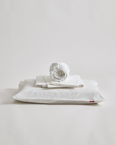 White cotton sheet set folded on a pillow by Iwata on a gray background