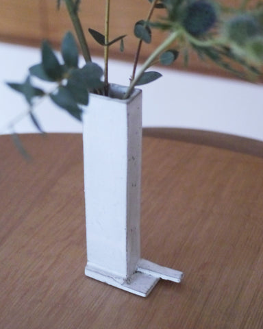 Close up in situation image of ceramic short white sculpture vase with foot with white overglaze by Masanobu Ando with eucalyptus on oak table. 