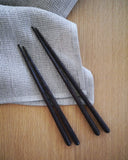 In situation image of set of hand carved tagaya wood children's chopsticks and regular chopsticks by Nalata Nalata on linen napkin against oak surface.
