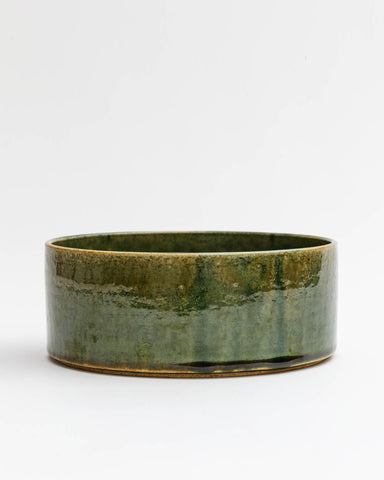 Silhouetted image of large ceramic oribe bowl with deep green glaze by Time and Style against white-gray background.
