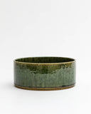Silhouetted image of ceramic medium oribe bowl with deep green glaze by Time and Style against white-gray background.