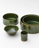 Image of small oribe bowl, stacked medium and large oribe bowls, oribe rice bowl, and oribe drinking vessel by Time and Style against white-gray background.