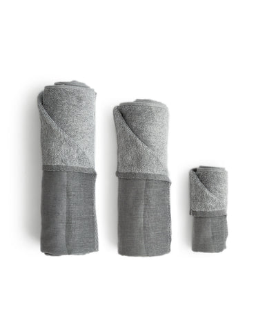 Silhouetted body, hand, and face zen charcoal towels rolled up placed next to each other, against white background.
