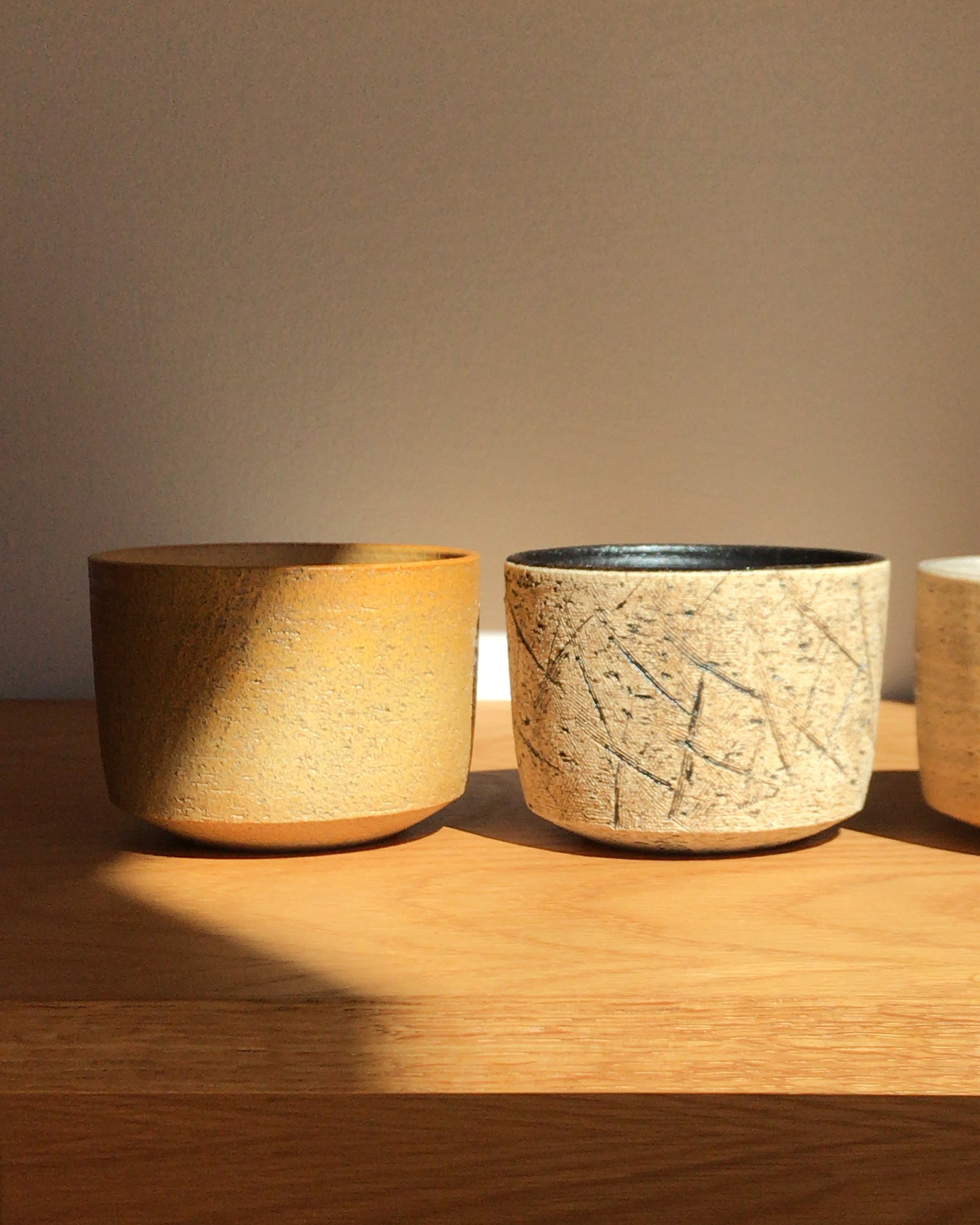 In-situation image of the kuro black matcha bowl next to otosai yellow matcha bowl on a wood shelf.